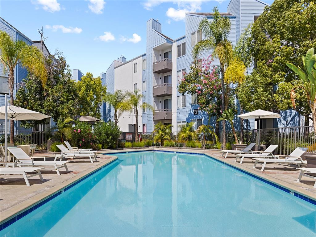 a swimming pool with chaise lounge chairs and umbrellas in front of an apartment building at Enclave, California, 90723