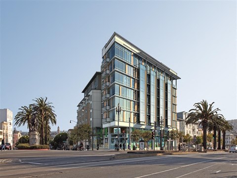 A modern building with glass windows is situated on a street corner with palm trees.