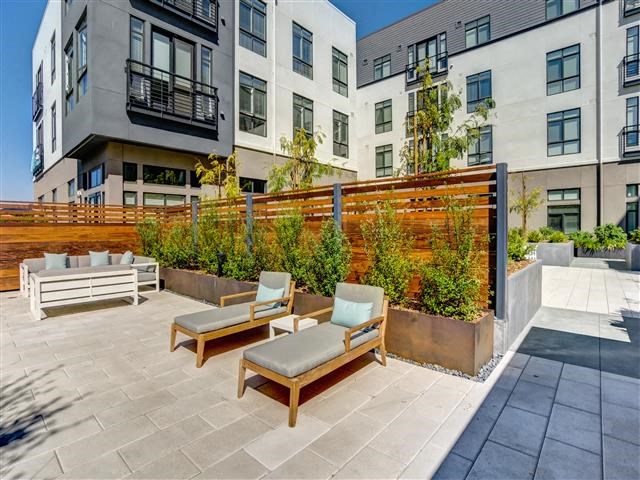 a patio with chairs and plants in front of an apartment building
