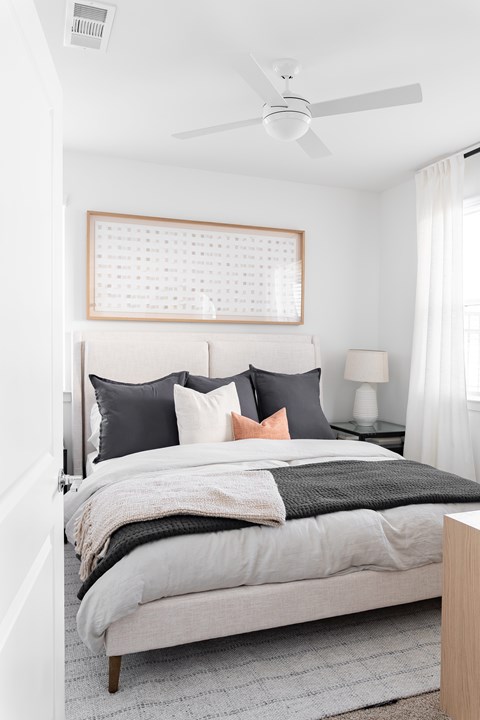 A bedroom with a bed, pillows, a fan, and a window.