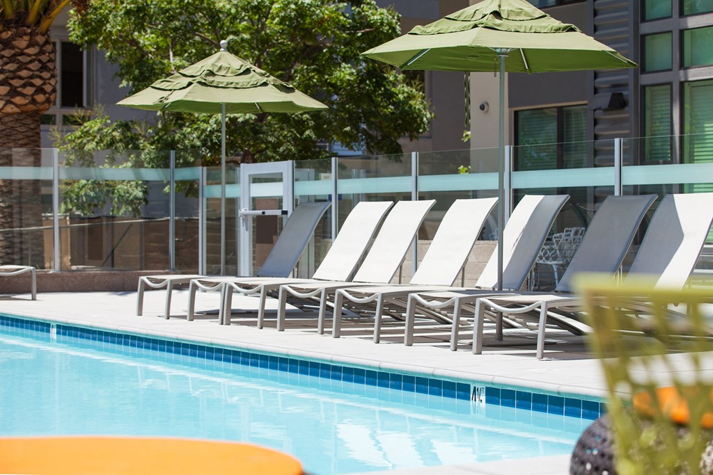 a pool with lounge chairs and umbrellas in front of a building