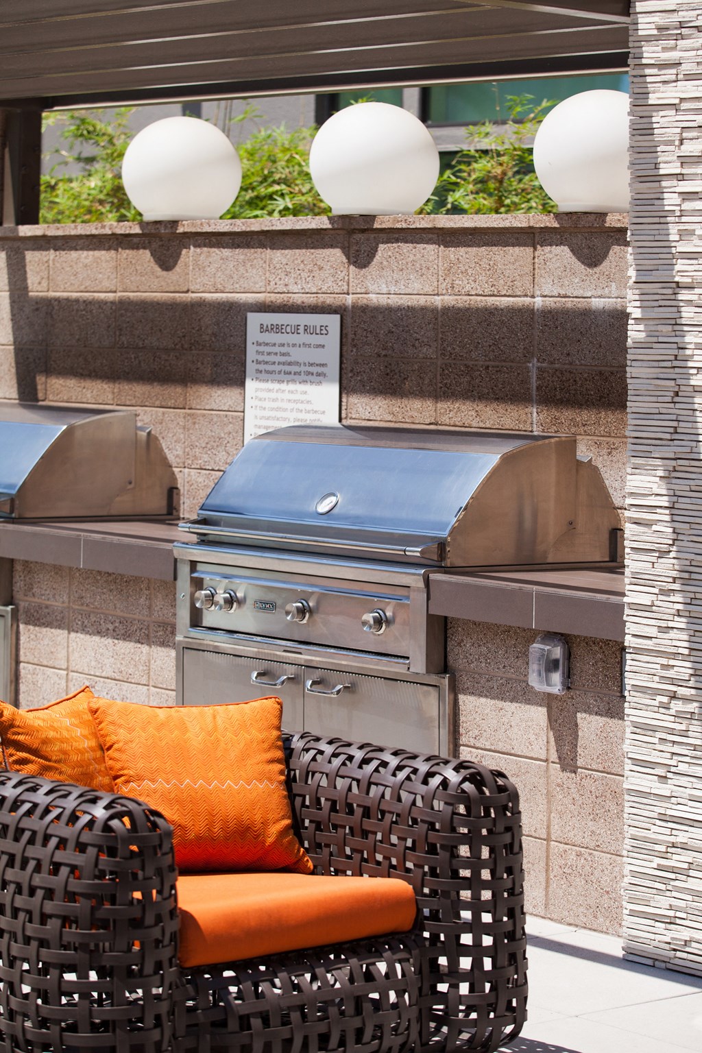 a bbq pit area with a wicker chair and orange cushions