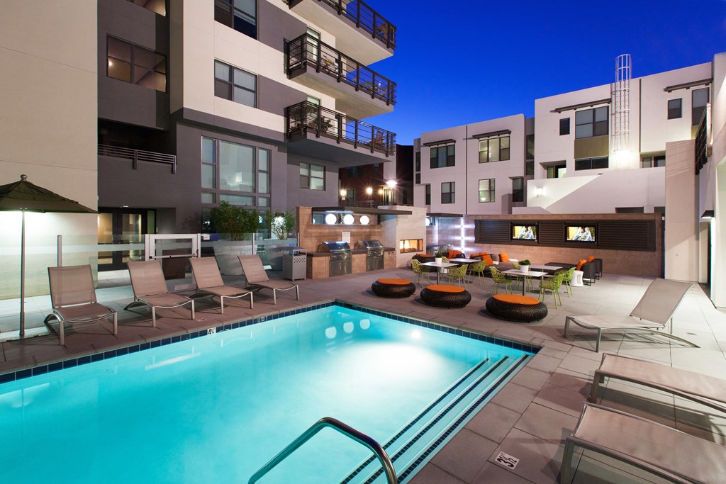 a swimming pool with lounge chairs and tables in front of an apartment building