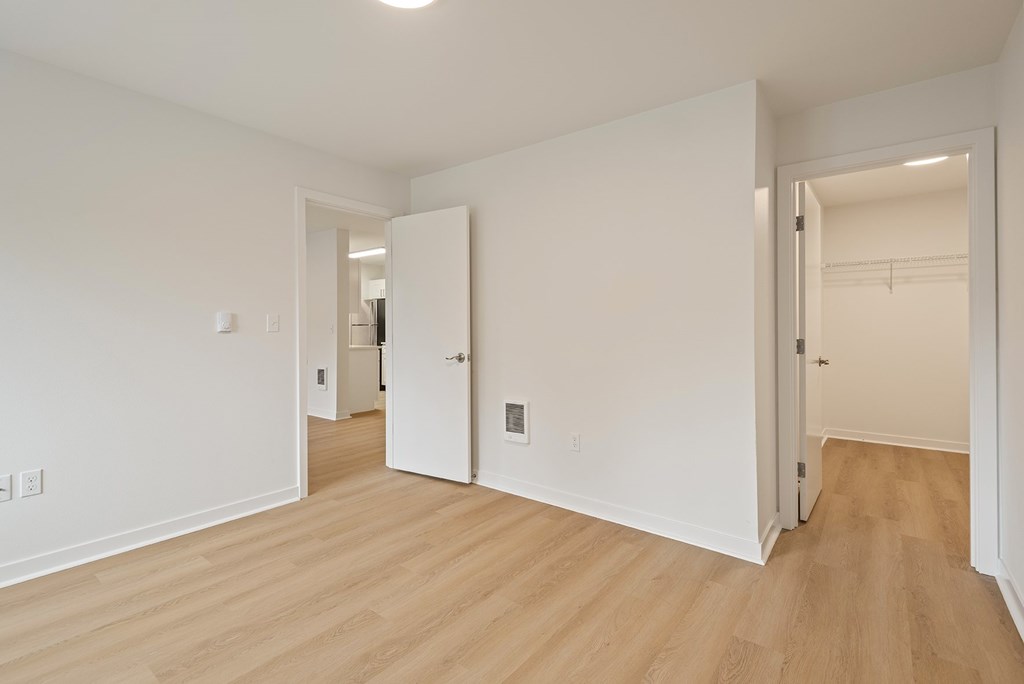 A room with white walls and wooden flooring with two open doors.