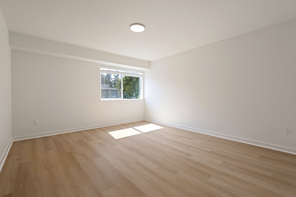 A room with wooden flooring and a window letting in sunlight.