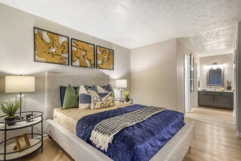A bedroom with a bed, a side table, and a painting on the wall.