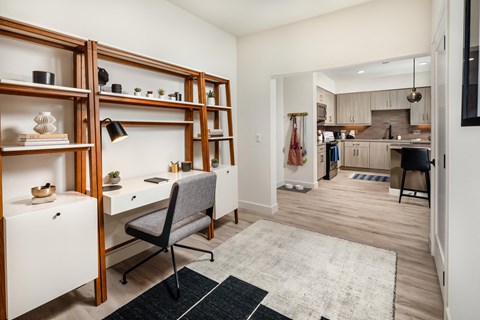 a home office area with a desk and a chair and a kitchen