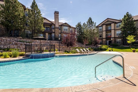 A swimming pool surrounded by a metal fence and a stone wall with a building in the background.