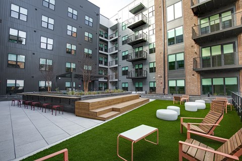 A modern courtyard with a grassy area, seating, and a building in the background.