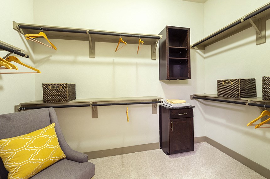 a walk in closet with shelves and hooks and a chair with a yellow pillow