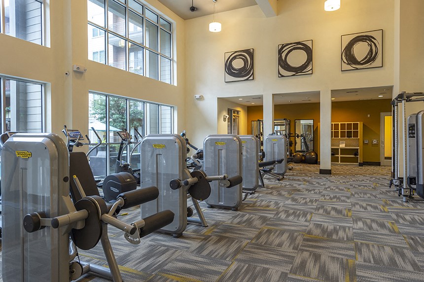 a gym with cardio equipment and weights in a building with large windows