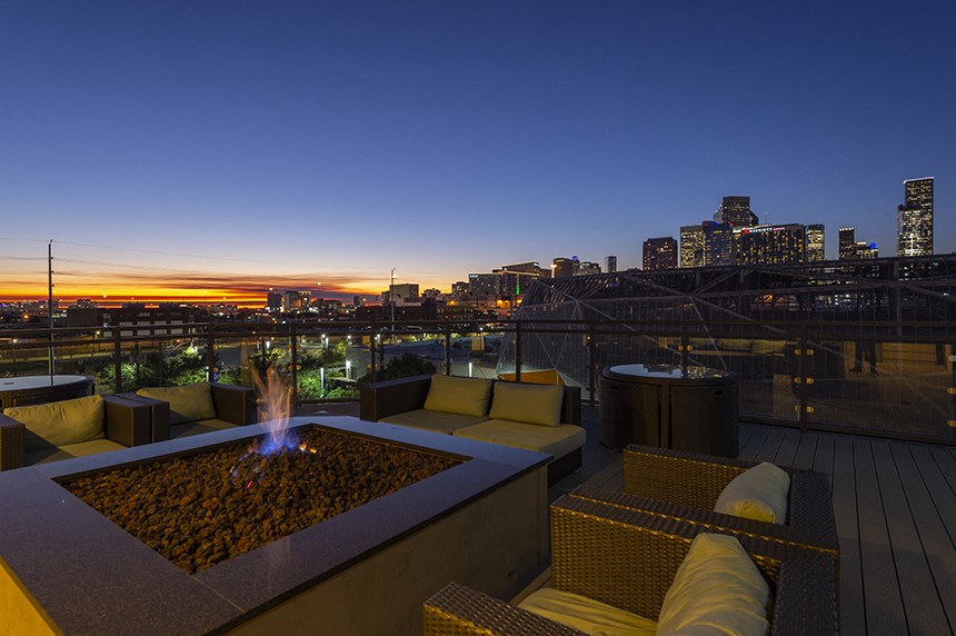 a rooftop deck with couches and a fire pit overlooking the city at sunset