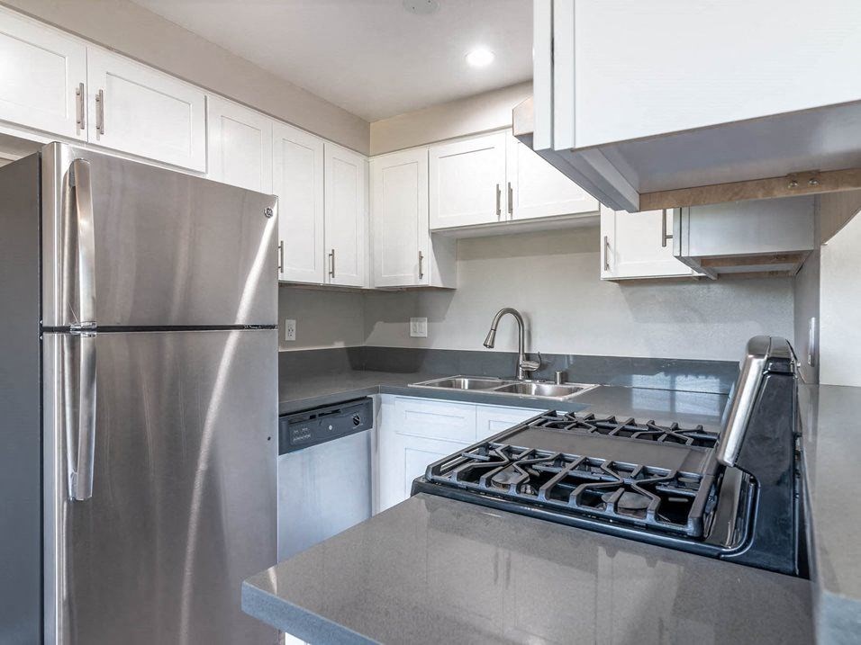 a kitchen with stainless steel appliances and white cabinets at Citrus Court Apartments, Whittier