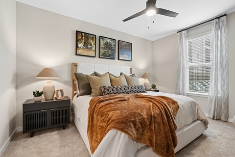 A bedroom with a bed covered in a brown blanket and a ceiling fan.