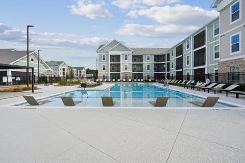 A swimming pool surrounded by lounge chairs and apartment buildings.