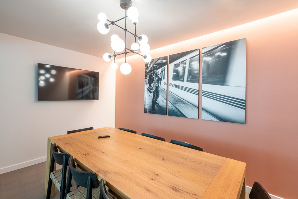 a long wooden table with chairs in a room with pink walls and a picture of a train
