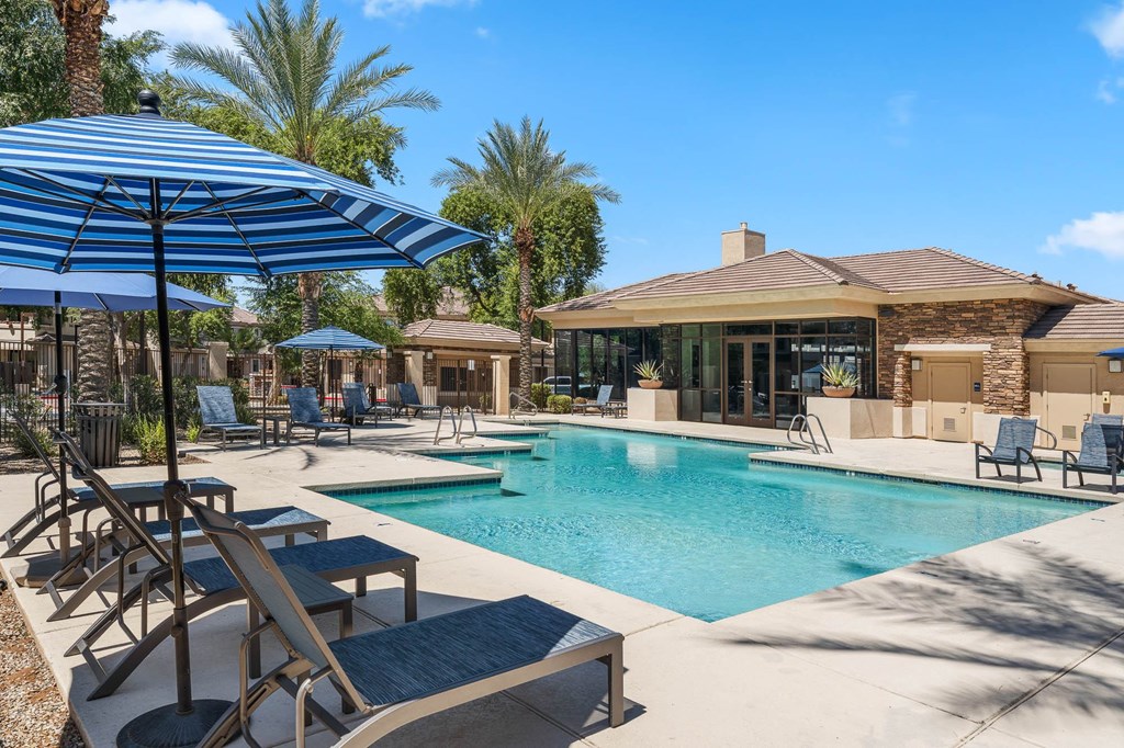 A pool area with a blue umbrella and lounge chairs.