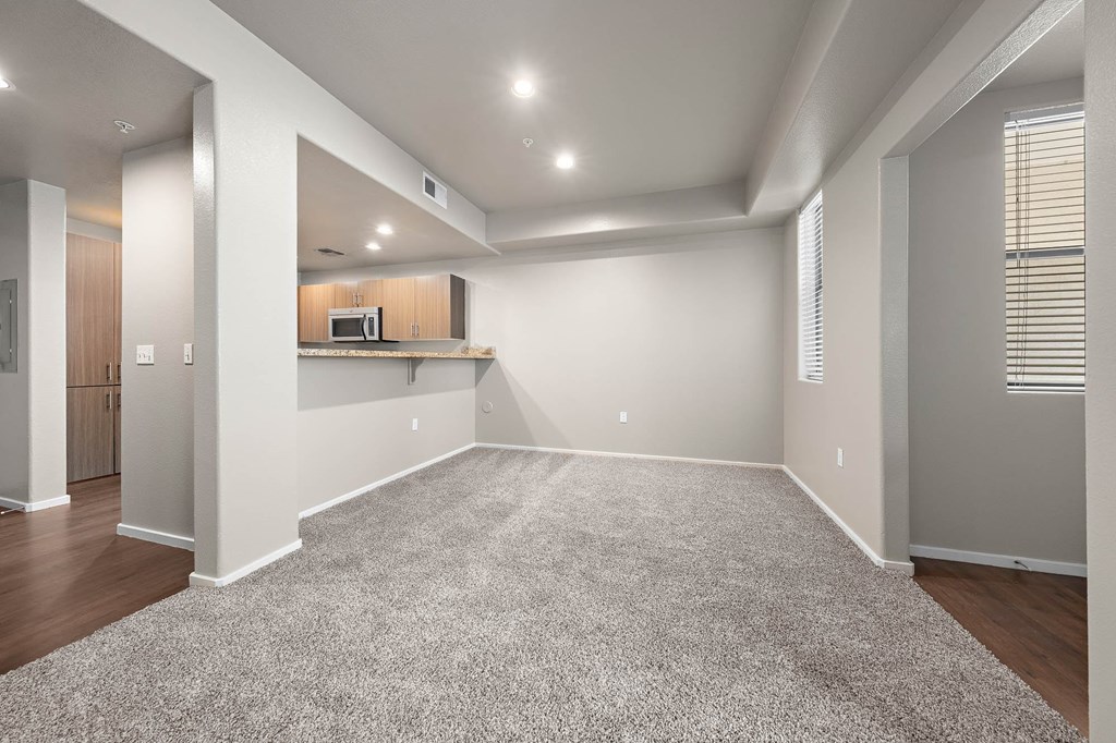 A spacious room with a carpeted floor and a kitchenette in the corner.