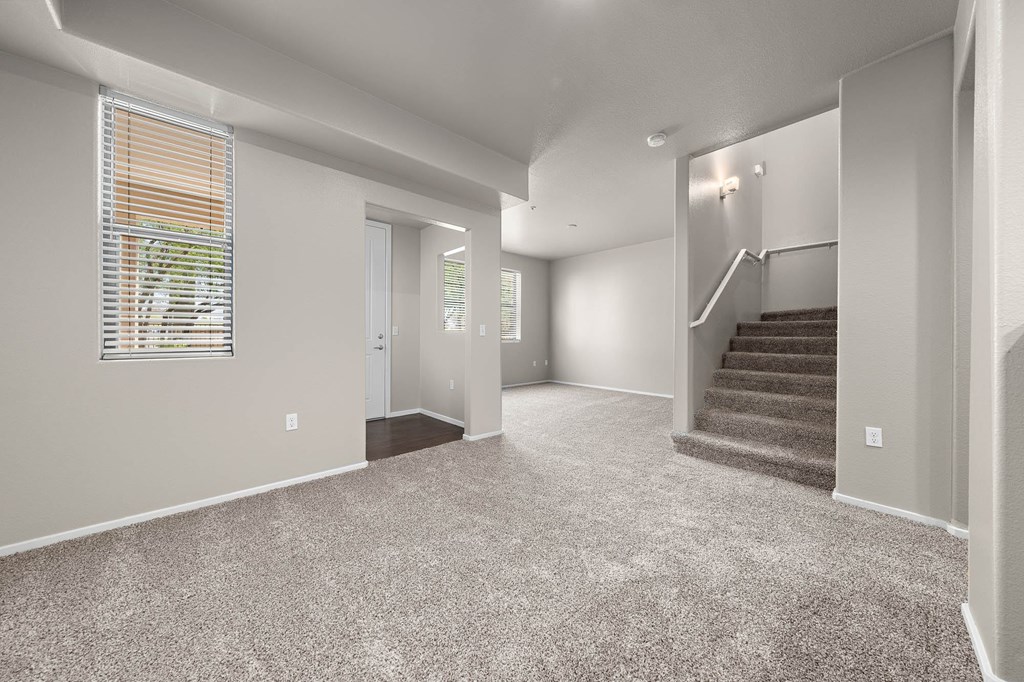 A spacious room with a staircase and a window with blinds.