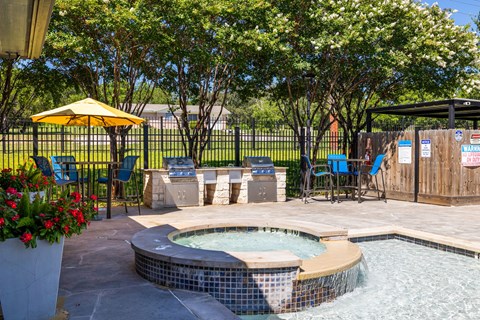 A small hot tub sits in the middle of a patio surrounded by chairs and a yellow umbrella at Clear Creek Meadows Apartments, Texas