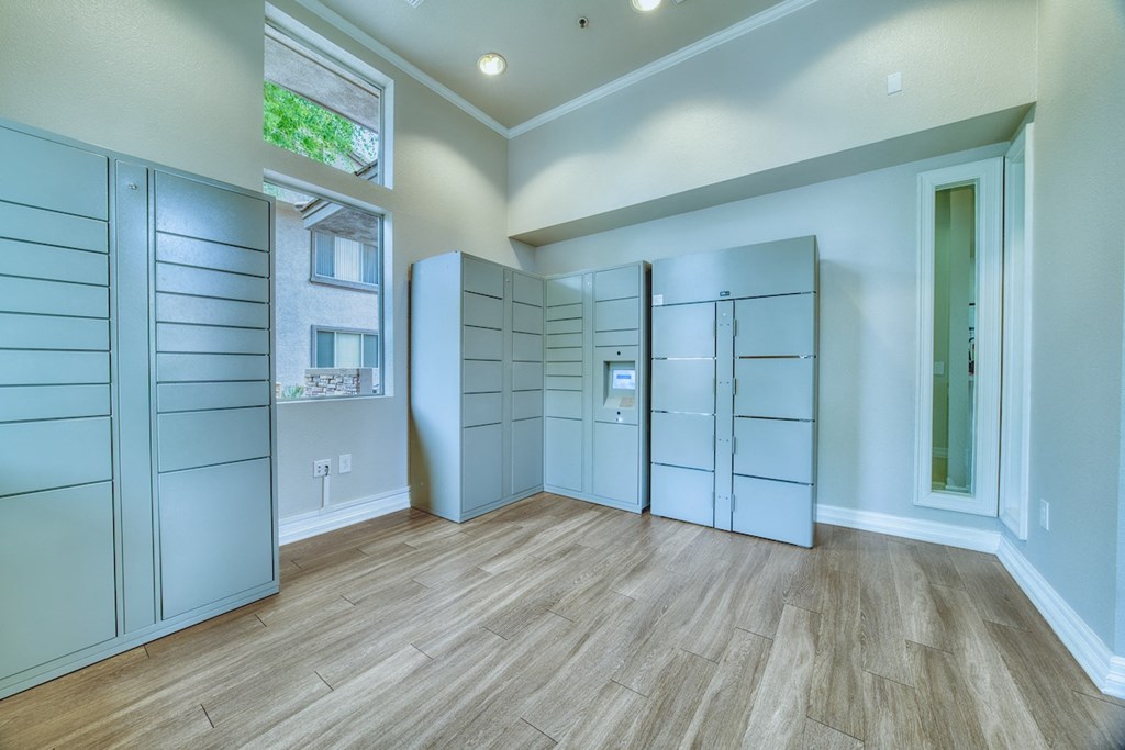 A room with wooden floors and white walls, featuring a row of white cabinets and a window.