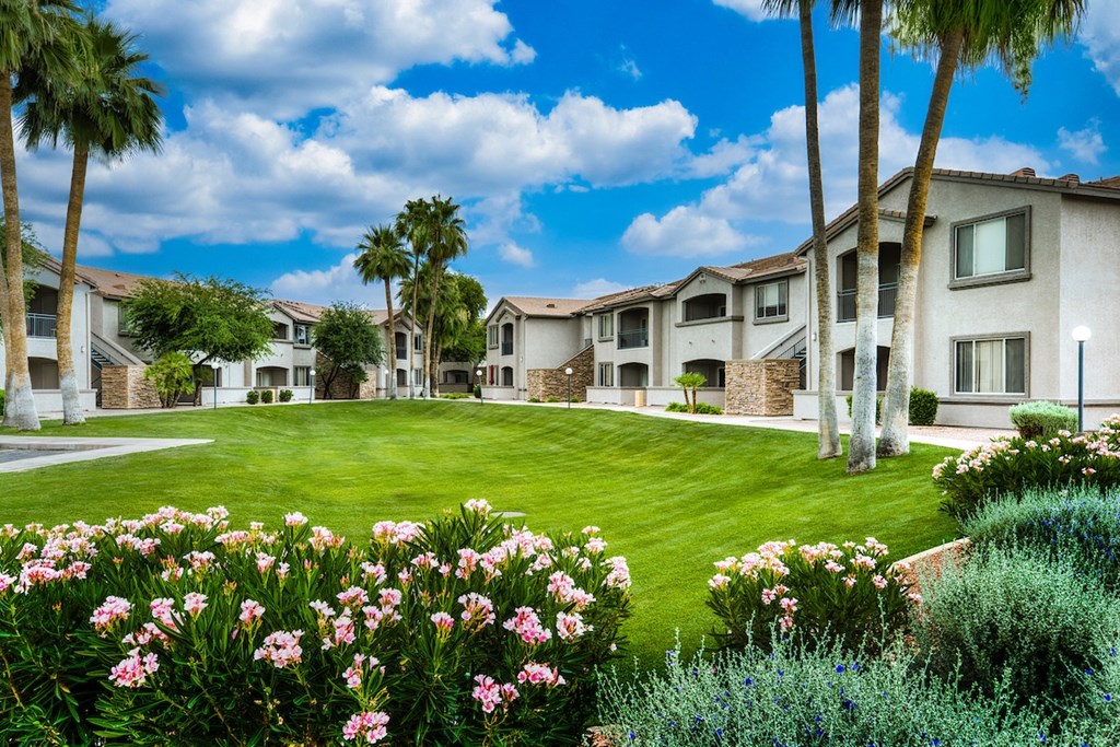 A sunny day at a residential complex with a well-maintained lawn and flowering plants.