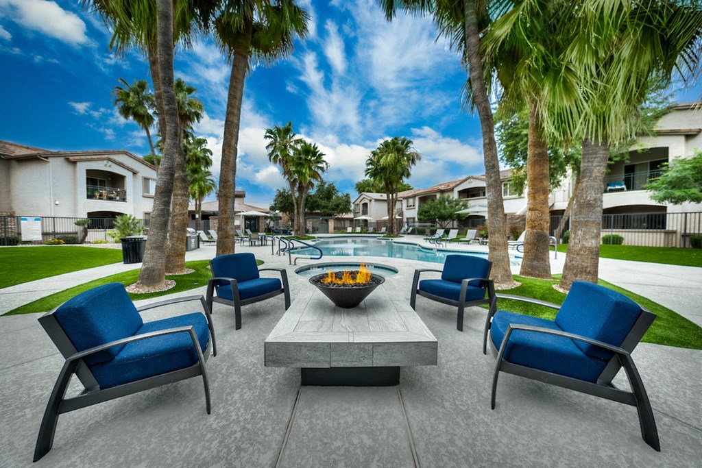 A patio with blue chairs and a fire pit surrounded by palm trees.