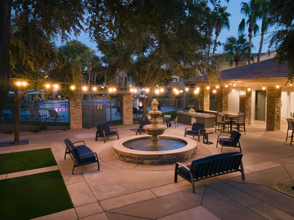 a fountain sits in the middle of a courtyard with seating and lights