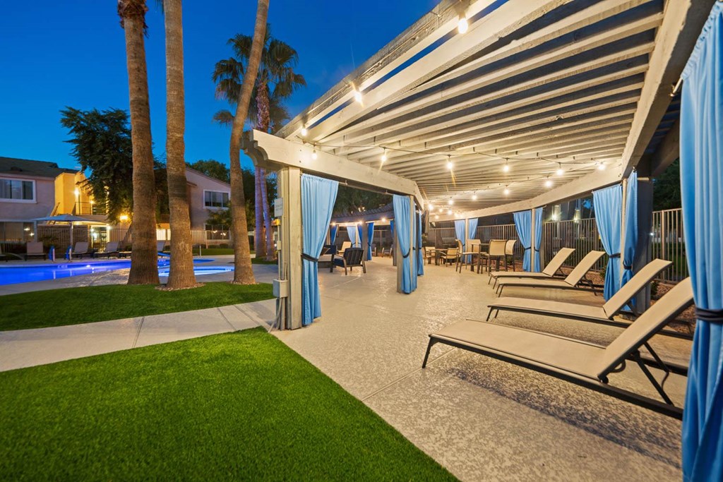 a patio with lounge chairs and a pool at night