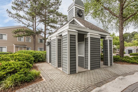 A small building with a clock tower sits in the middle of a brick walkway.
