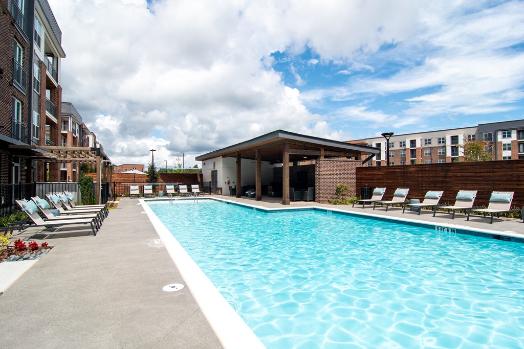 a swimming pool with chaise lounge chairs and a pavilion in front of a brick building