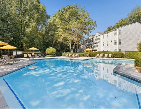 A large swimming pool surrounded by trees and lounge chairs.