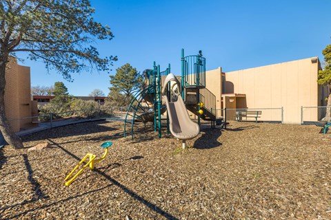 A playground with a yellow seesaw and a green slide.