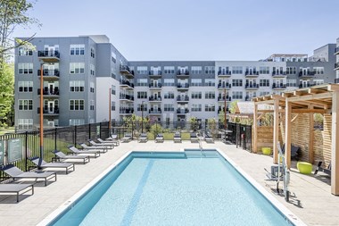an outdoor pool with lounge chairs and a pergola at the preserve at great pond apartments