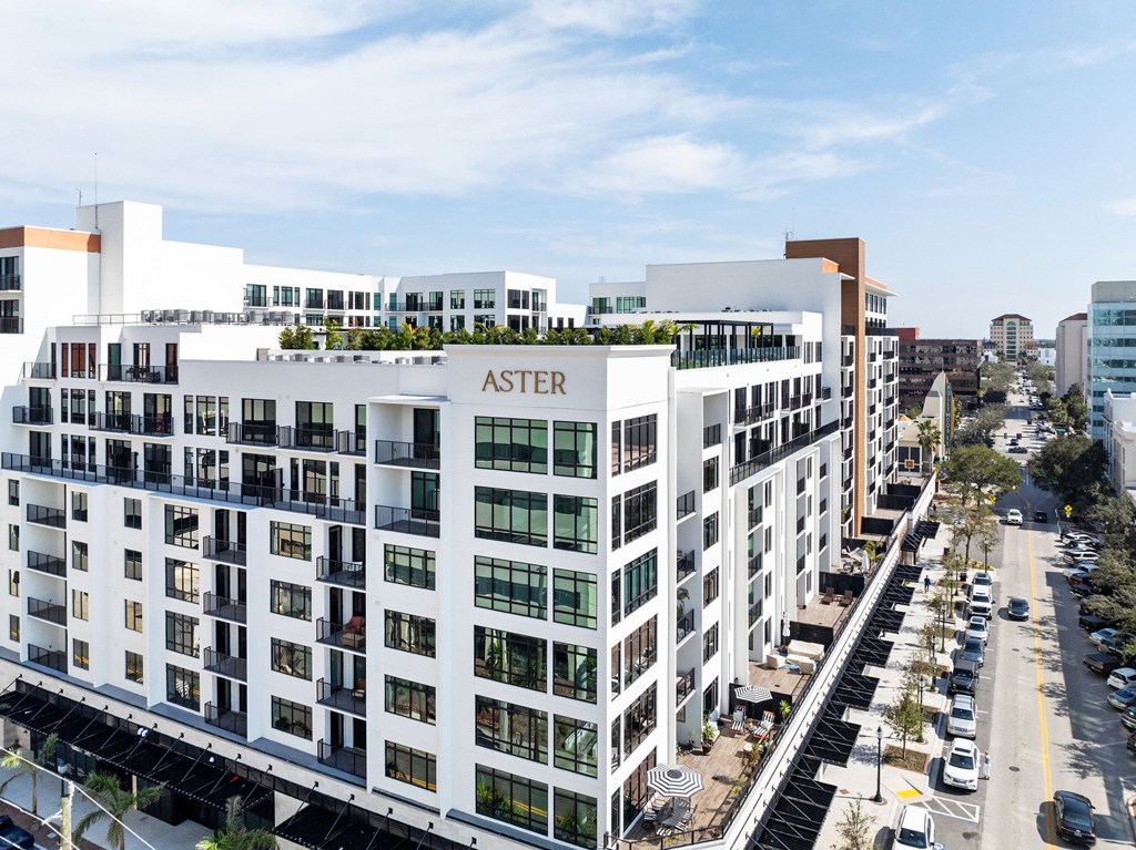 A white building with the word "ASTER" on the side is surrounded by other buildings and a parking lot.