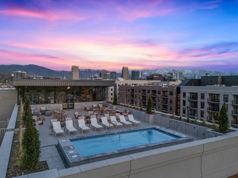 A rooftop pool area with lounge chairs and a view of the city skyline at sunset.