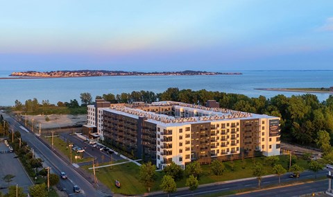 A large apartment complex is situated on a road with a body of water in the background.