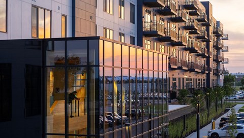 A modern building with balconies and large windows is shown during sunset.