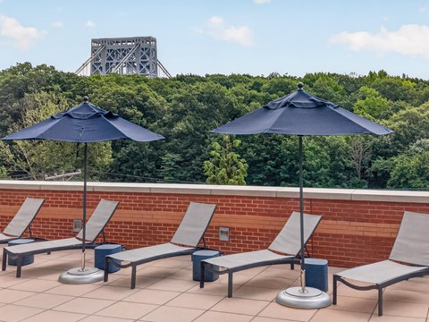 A set of four chairs and two umbrellas are on a patio with a bridge in the background.