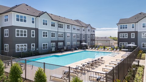A large swimming pool is surrounded by sun loungers in front of apartment buildings.