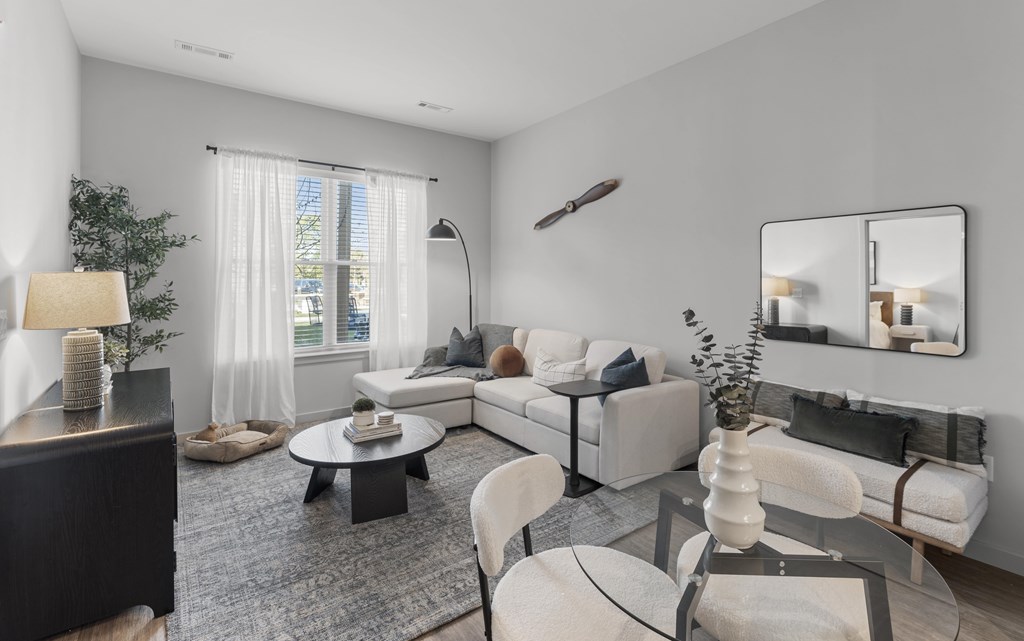 A modern living room with a white sofa, a glass coffee table, and a large mirror on the wall.