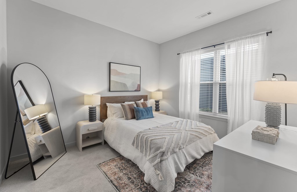 A bedroom with a large bed, a side table with a lamp, and a mirror.