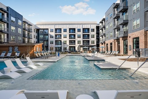 A swimming pool surrounded by lounge chairs and buildings.