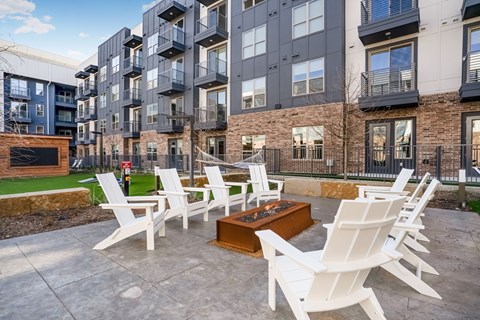 A patio with white chairs and a fire pit in front of apartment buildings.