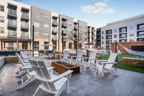 A patio with white chairs and a table in front of apartment buildings.