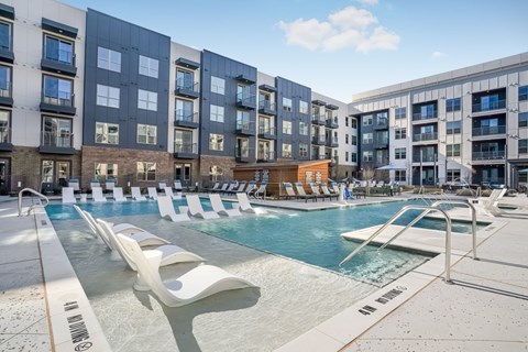 A swimming pool with lounge chairs in front of apartment buildings.