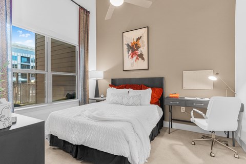 A bedroom with a large bed, a desk with a chair, and a window with a view of a building outside.