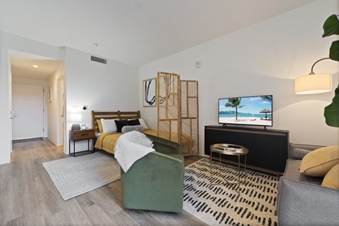 A modern living room with a grey sofa, a green armchair, a wooden side table, and a television displaying a beach scene.