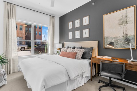 A bedroom with a large bed, a desk with a chair, and a painting on the wall.
