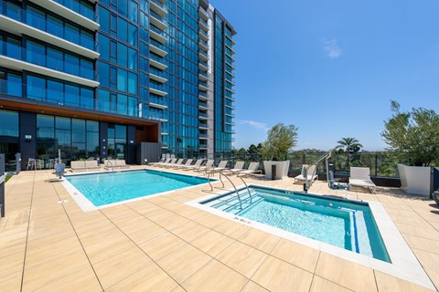 A large outdoor swimming pool surrounded by lounge chairs and a tall building in the background.